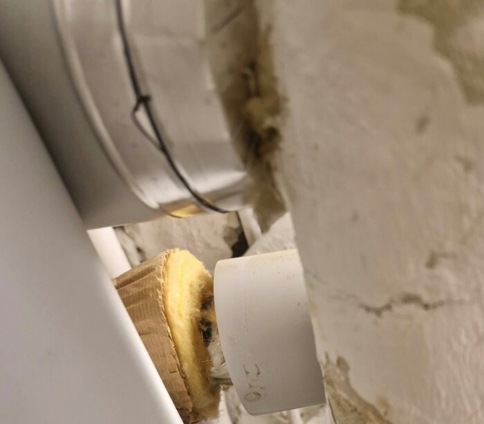 Gammalt rör med isoleringsmaterial, potentiellt misstänkt för asbest eller annan hälsovådlig substans, omgiven av vitmålad yta.