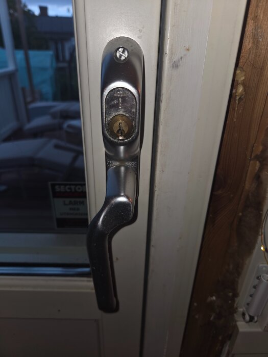 Trasigt handtag på altandörr, sitter fast med envägsskruvar, låscylinder synlig.