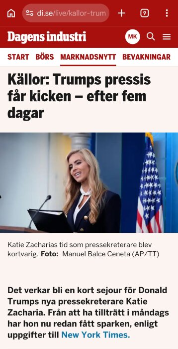Kvinna vid talarstol med amerikansk flagga i bakgrunden, ler och håller mapp, presskonferensrum.