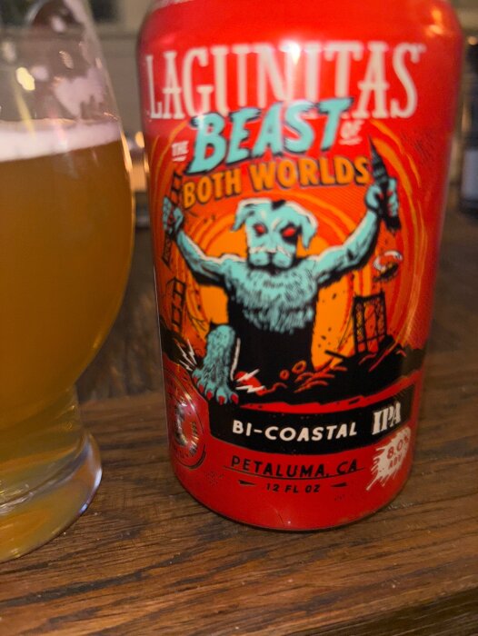 Burk med Lagunitas "The Beast of Both Worlds" Bicoastal IPA och ett fullt glas öl på ett träbord.