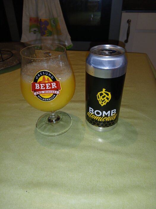 En burk med texten "Bomb Atomically" bredvid ett glas med orange öl från Öresund Beer and Whisky Festival.