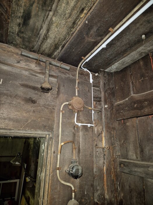 Gammal svart lampknapp demonterad och ny vit lampknapp installerad på trävägg i utehus. Rör och elledningar synliga i bilden.
