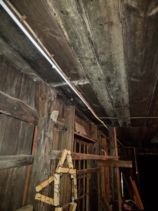 Uthus med träväggar och tak, visar nyinstallerad vit lampknapp och bortkopplad svart knapp. Eldragning längs taket syns.