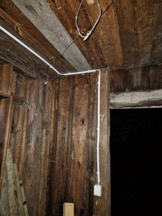 Vit lampknapp på grov trävilla med synlig kabelinstallation i hörnet.