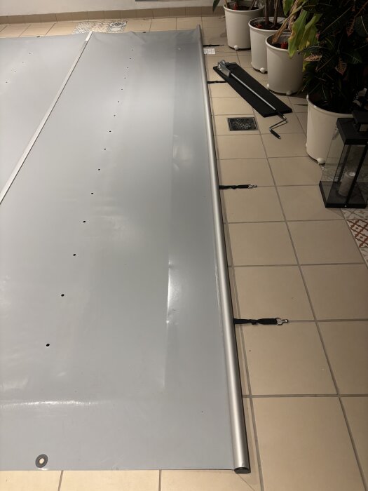 Grå matta med uppfällningssystem på klinkergolv, omgiven av växter i krukor.