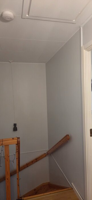 Trappuppgång med en lucka till vinden i taket och en träledstång längs väggen.