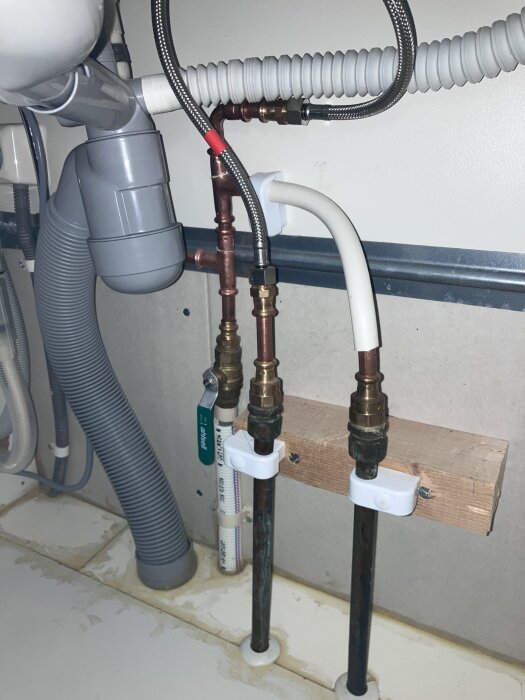 VVS-installation med rör och slangar under diskbänk, inkluderar vattenfilter och avloppsanslutning.
