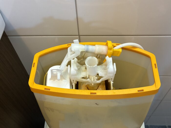 Inuti av en äldre toalettcistern med mekanismer, synlig gulnad plast och vattenfylld tank.