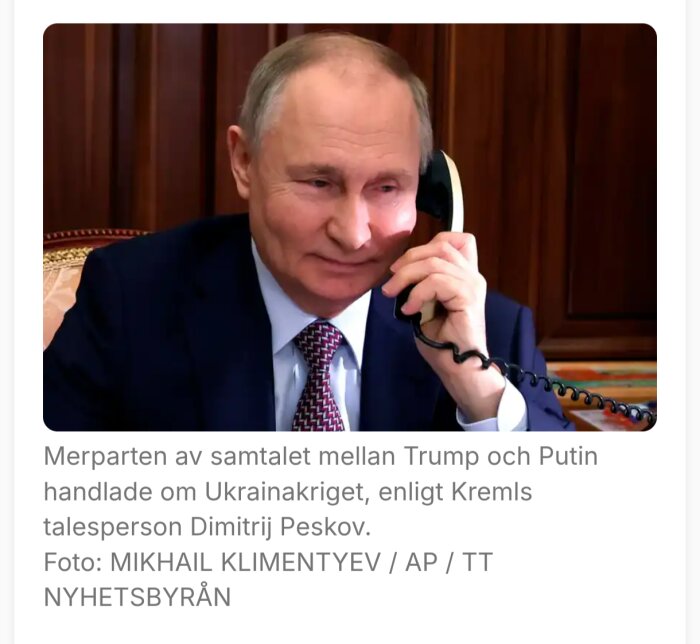 En man i kostym pratar i telefon i ett kontor med träpaneler i bakgrunden.