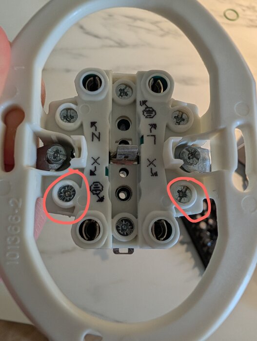 Skruvar markerade med röda ringar på en vit elektrisk komponent, potentiellt kopplingspunkt för kablar.