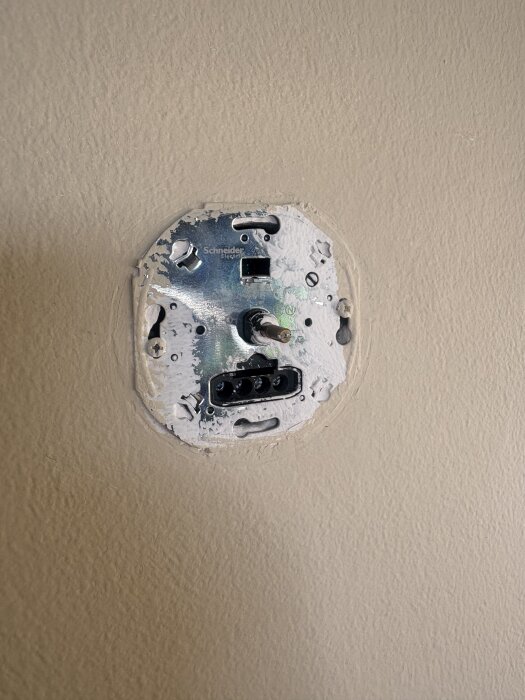 Inbyggd strömbrytare av metall på en vägg, avsedd för installation av en dimmer eller knapp, med synliga kabelfästen.
