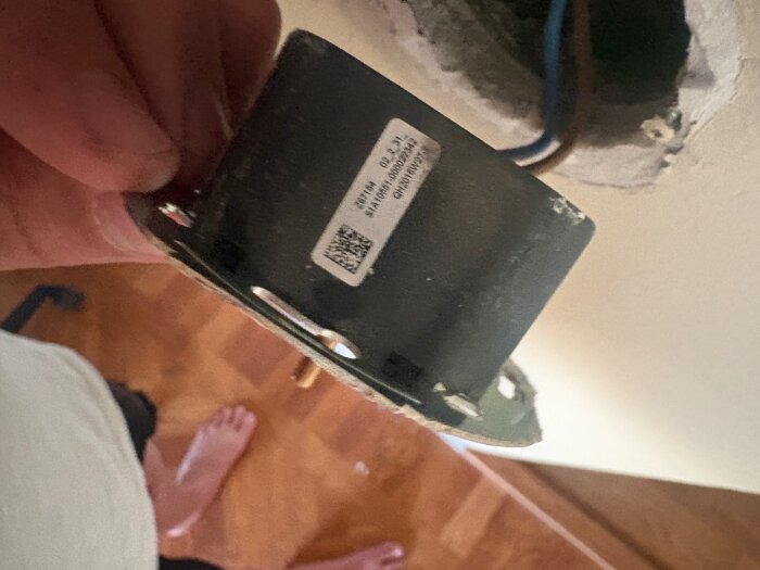 En hand håller i en losskruvad elektrisk komponent mot en vägg, troligen en del av en dimmerinstallation.