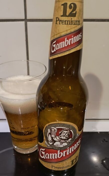 Flaska och glas med Gambrinus 12 Premium tjeckisk pilsner, ett gyllene öl med skumkrona.