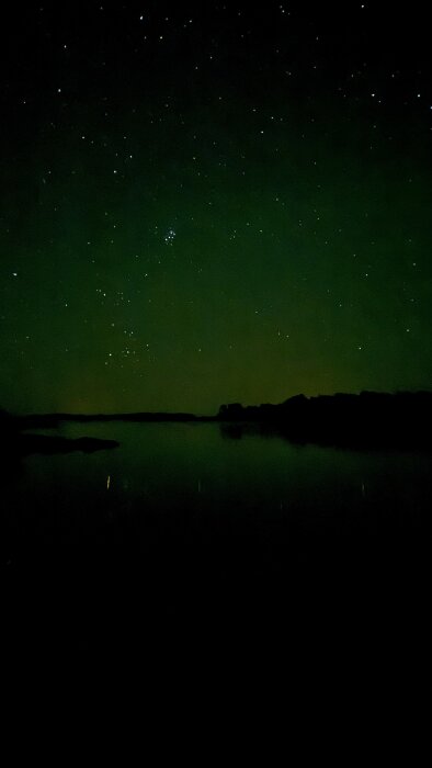 Nattfoto av stjärnhimmel över havet, silhuetter av öar och svagt grönskimrande himmel i bakgrunden.