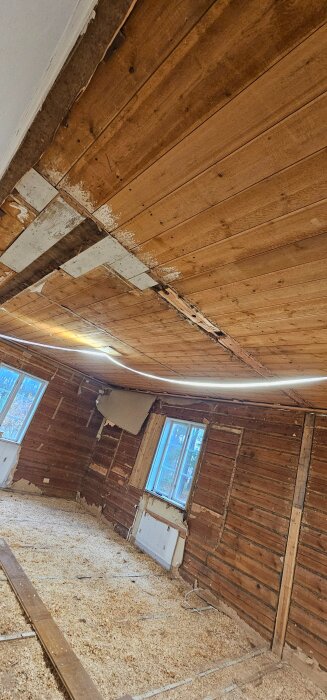 Renovering av gammalt timmerhus med exponerade väggar och tak i trä. Spånskivor på golvet, fönster mot vägg.