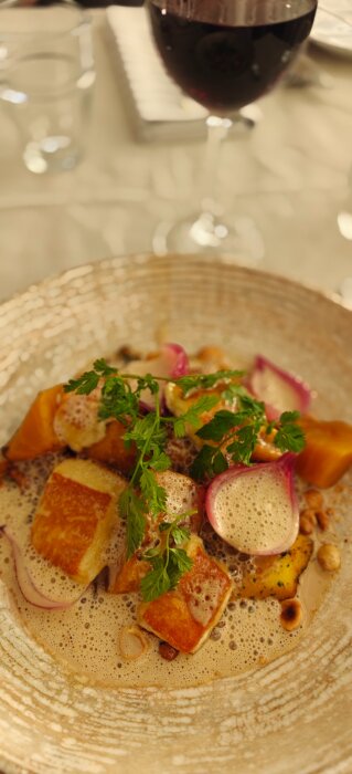 Kantarellgnocchi serverad på en keramikplatta med skummig sås och gröna örter, med ett glas rödvin i bakgrunden.