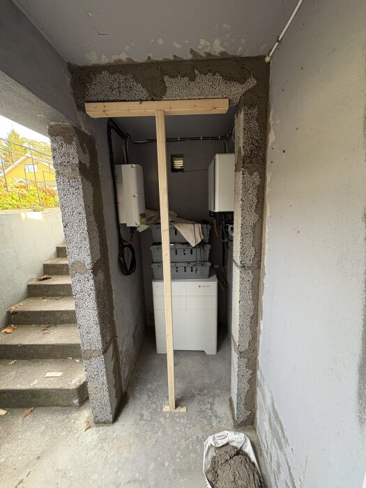 Utrymme under renovering med murade väggar och Lecablock, en ståldörr in ska monteras. Väggmonterade växelriktare och batterilådor syns.