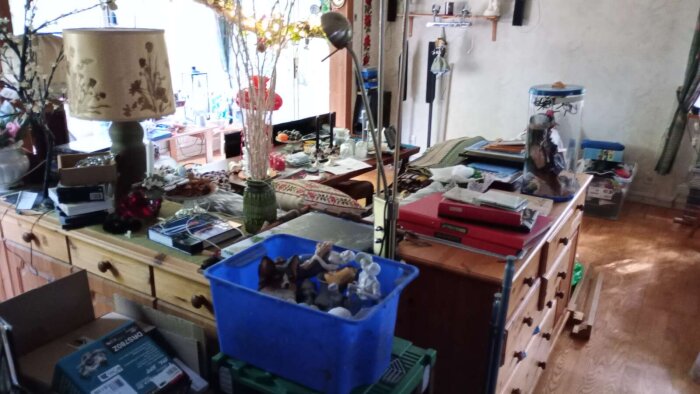 Överbelamrad inomhusmiljö med prylar på möbler, inklusive lampor och lådor, symboliserar hem hos en hoarder före rensning och renovering.