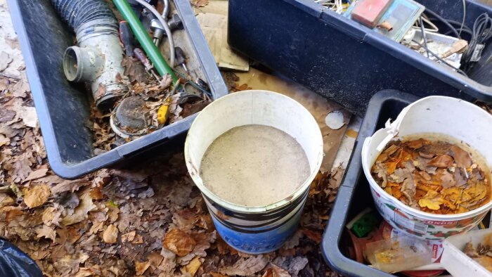 Behållare fyllda med löv och skräp i ett stökigt förråd med diverse verktyg och tillbehör bland höstlöv.