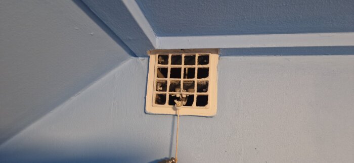 Gammal vit ventilationslucka i ett blåmålat rum, kanske relaterad till luftcirkulationsproblem i en vind.