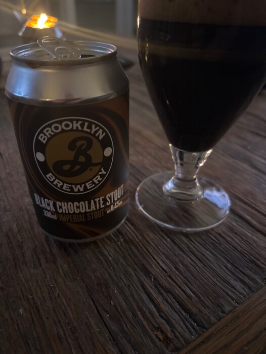 Burk med stout och ett glas på ett träbord, ljus i bakgrunden.