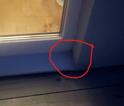 Suddig bild av ett område vid en dörrkarm med fokus på hörnet och golvet. Röd cirkel markerar intresset i området.