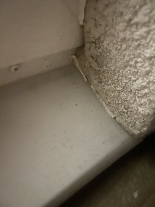 Spricka i ett hörn mellan en slät yta och en grov yta, troligen inomhus vid ett fönster eller dörrkarm.