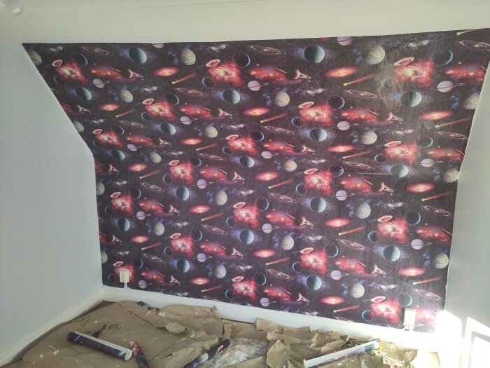 En fondtapet med rymdmotiv uppsatt i rum 5. Golvet är täckt med papper och verktyg, troligen från pågående renovering.