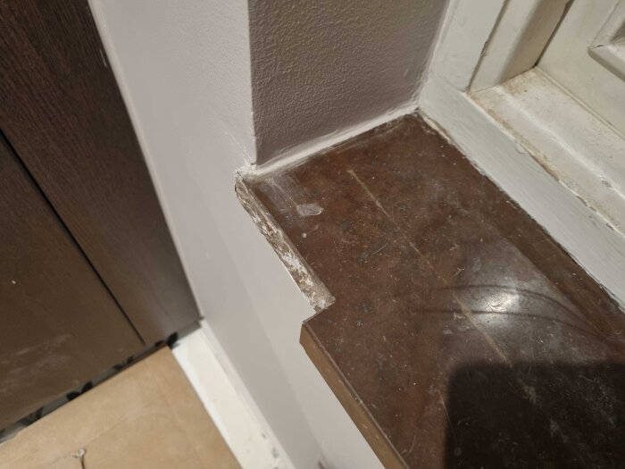 Bilden visar en brun marmorskiva vid ett fönster med en bortskuren del, eventuellt för att ge plats åt ett köksskåp. Skivan har synliga repor.