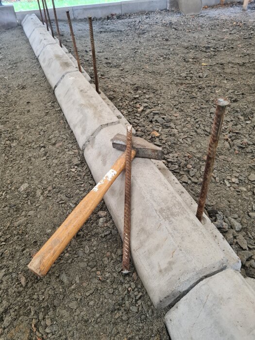 Kantsten med armeringsjärn ned i gruset; en hammare och ett armeringsjärn ligger på stenarna, omgivna av en grusyta.