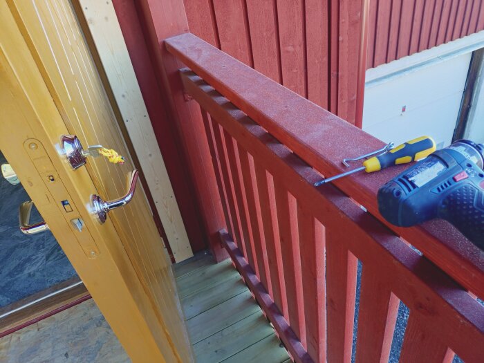 Ytterdörr med monterad hasp, omgiven av träpanel och verktyg som skruvmejsel och borrmaskin.