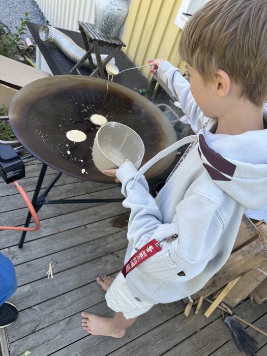 Pojke i huvtröja häller smet på en stekhäll utomhus, två plättar syns.