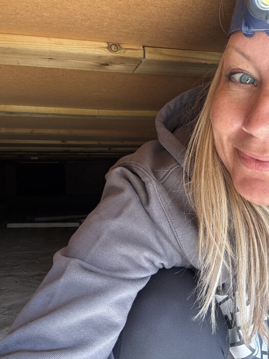 Person med pannlampa kryper i ett trångt utrymme med träbeklädda väggar och tak.