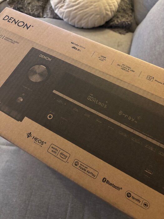 En kartong med en Denon-ljudanläggning, inkluderar Dolby Atmos, DTS:X, och stöd för Alexa, Apple AirPlay, Bluetooth och Spotify.