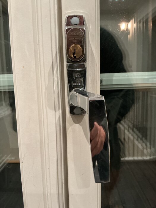Altanhandtag och låskolv på en äldre altandörr, med reflektioner i glaset och ett slitet utseende.