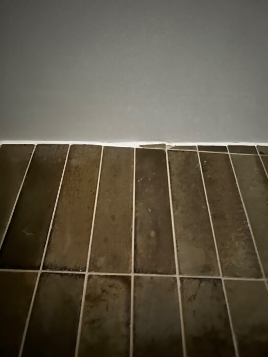 Ojämt kapade kakelplattor i översta raden mot taket i ett badrum, med varierande glipor och antydd trappstegseffekt.