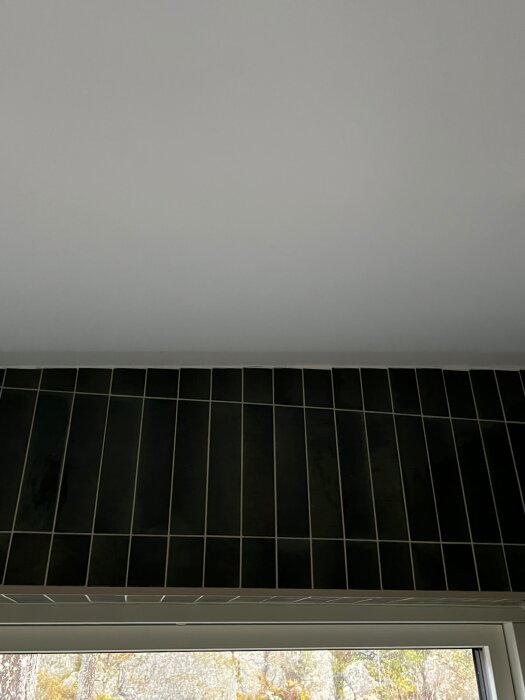 Badrumsvägg med svarta kakelplattor mot tak, ojämnt kapade plattor orsakar varierande glipor och trappstegseffekter vid taket.