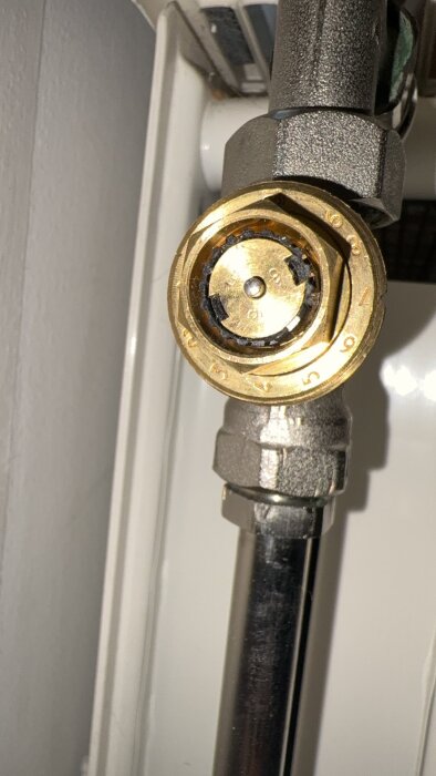 Närbild på en termostatventil på ett rör till en radiator, med fokus på den mässingsfärgade justeringsratten.