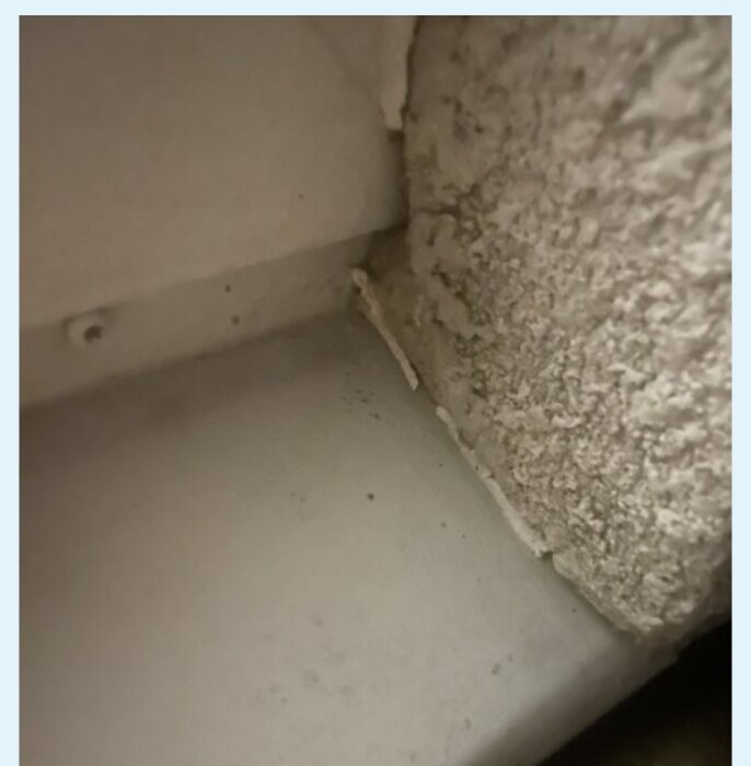 En bortnött fog mellan fönsterkarm och puts, med synligt slitage och påbörjad skada vid fönsterblecket.