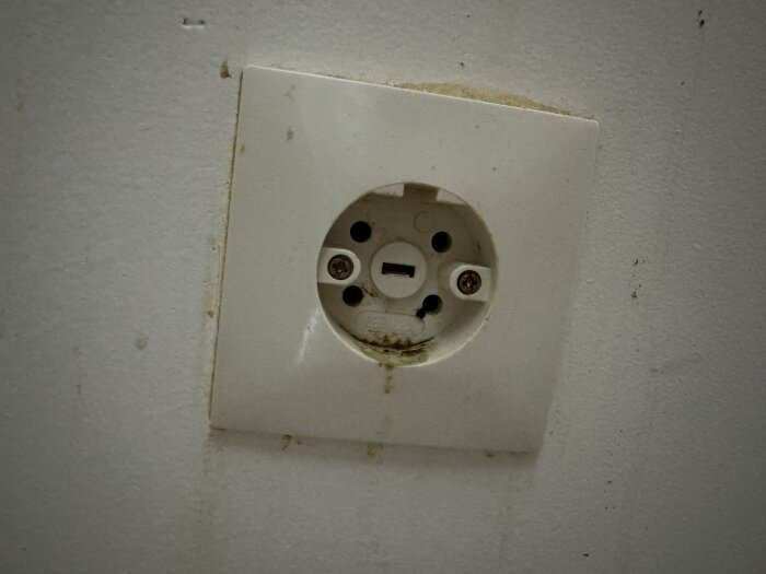 Vit väggkontakt med smuts och gulnande fläckar, sedd framifrån, monterad i vägg.