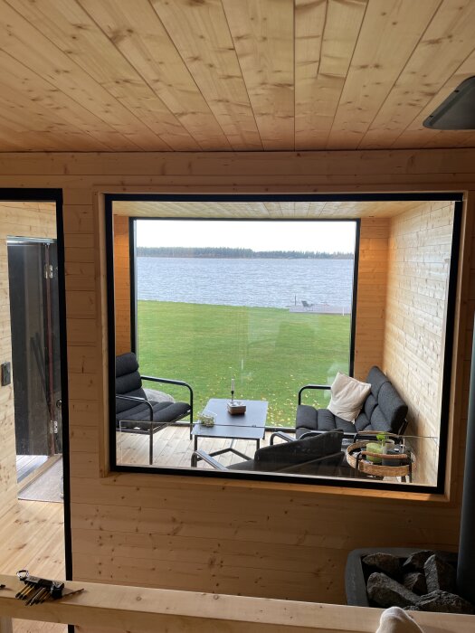 Utsikt från bastu mot inglasad veranda med sittgrupp, bord och sjövy.