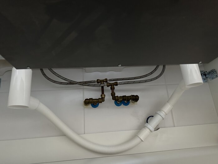 Flexibelt avloppsrör under handfat med extra vattenlås och röranslutningar, kopplade under sned vinkel till vägghål vid ett badrumsskåpsinstallation.