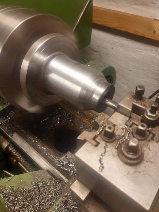 En metallcylinder bearbetas i en svarv, omgiven av metallspån och verktyg, under tillverkning av en elmotoradapter.