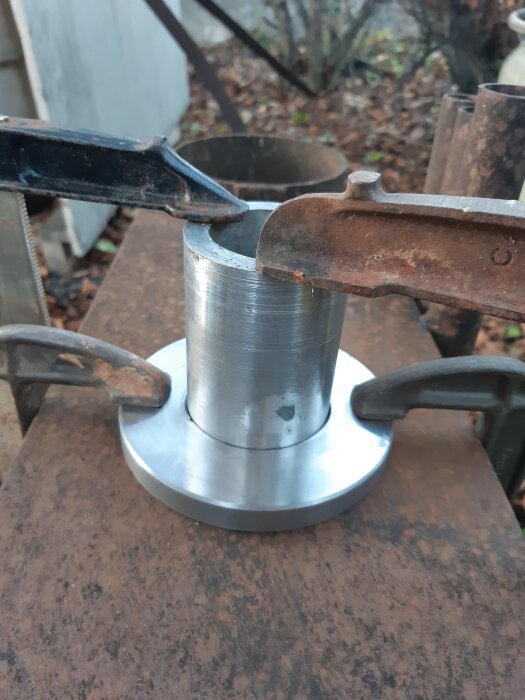 Cylindrisk metallkomponent fastspänd i ett skruvstäd, del av en adapter för att montera en elmotor på en Bergma bergborrslipmaskin.