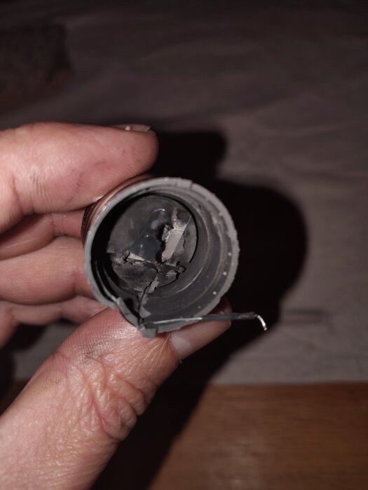 Trasig LED-lampa som lossnat i bitar, visar tecken på brännskador och skador i transformatordelen, hålls i hand.