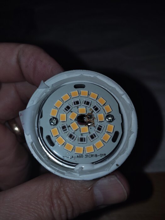 Skadad LED-lampa med överhettad transformatordel, vissa delar brända och lossnade under demontering, hålls i handen för närmare undersökning.