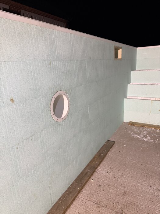 Poolvägg med monterad lampa och öppning för skimmer i kvällsbelysning, omgiven av en betongyta, klar för gjutning.