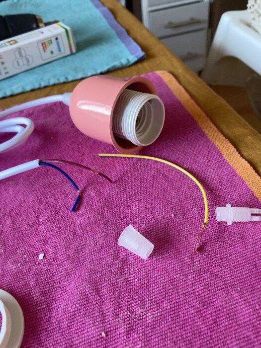 Lampsockel och sladdar på en rosa textilbakgrund, med förpackningar i bakgrunden.