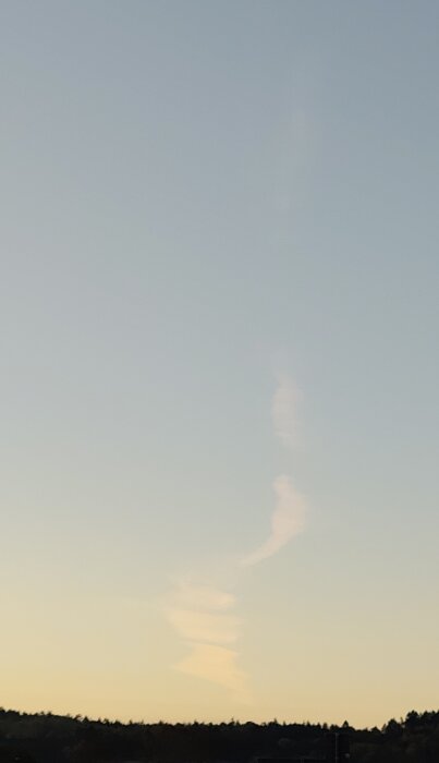 Kondensstrimma på himlen vid solnedgång, liknar ett konstverk.