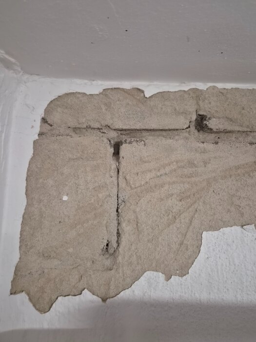 Spricka och lagning i källarvägg av lättbetong, horisontell fog mellan block, synligt utanför bild. Missfärgat murbruk, smulande puts.